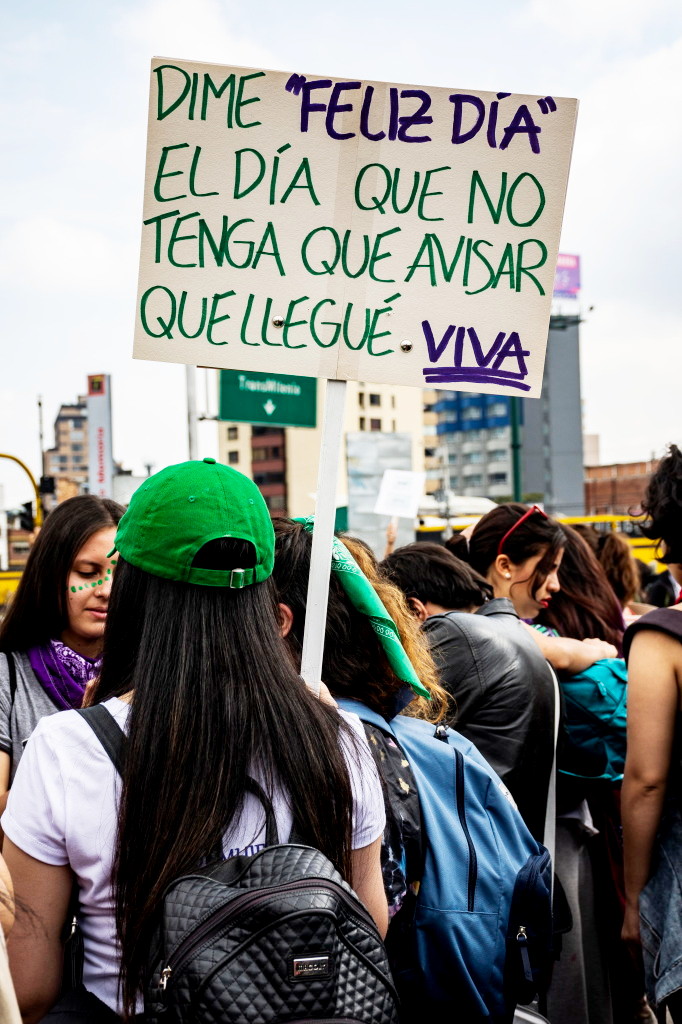 Mujeres reunidas, una de ellas lleva un cartel que dice: "Dime 'feliz día' el día que no tenga que avisar que llegué viva". Foto: Leidy Benítez