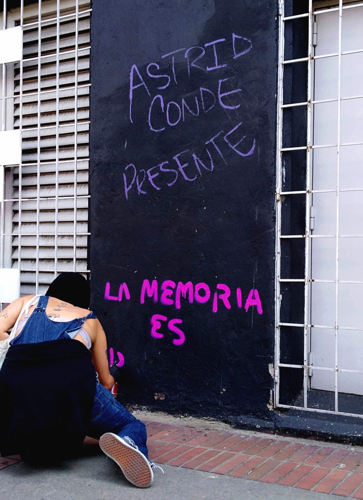 Mujer pinta un grafiti que dice: "Astrid Conde presente, la memoria es...". Foto: Andrea Umaña