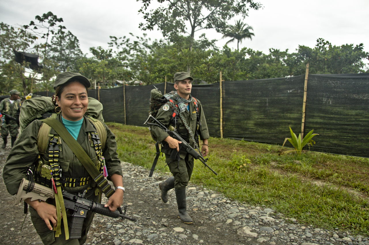 Una mujer sonriente y un hombre encabezan una fila de excombatientes que caminan hacia el punto de dejación de armas. Foto: Andrés Gómez.