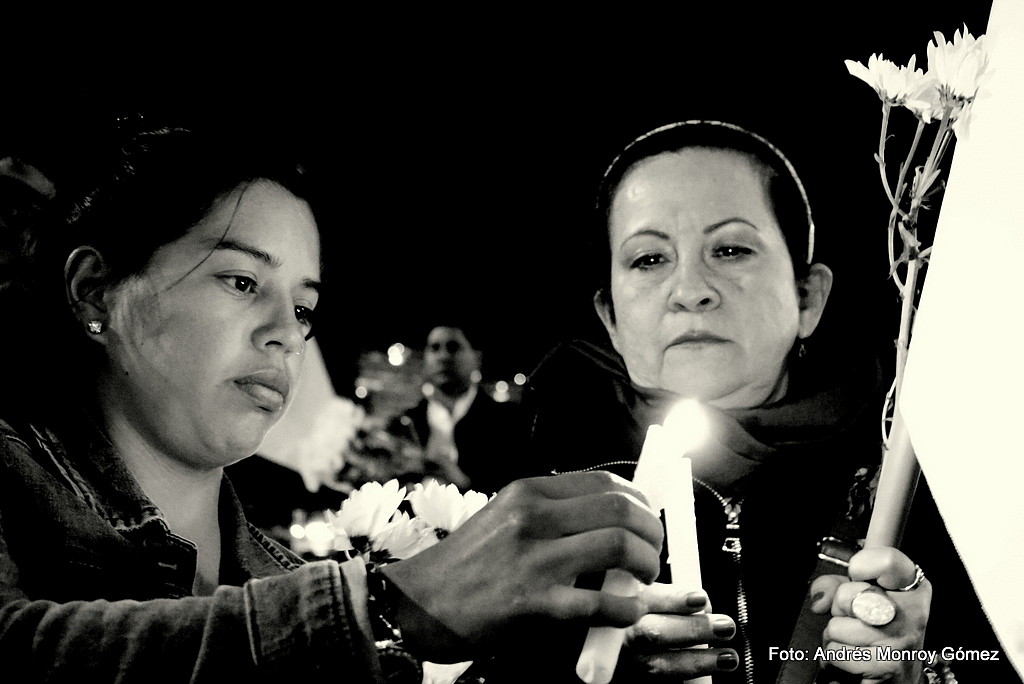 Dos mujeres encienden velas, una de ellas sostiene una bandera blanca. Foto: Andrés Monroy Gómez.