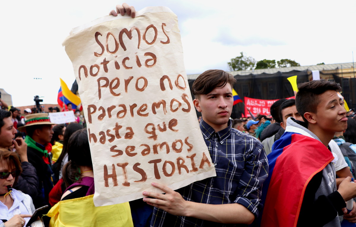Un joven en una protesta sostiene un cartel que dice: "Somos noticia, pero no pararemos hasta que seamos historia"