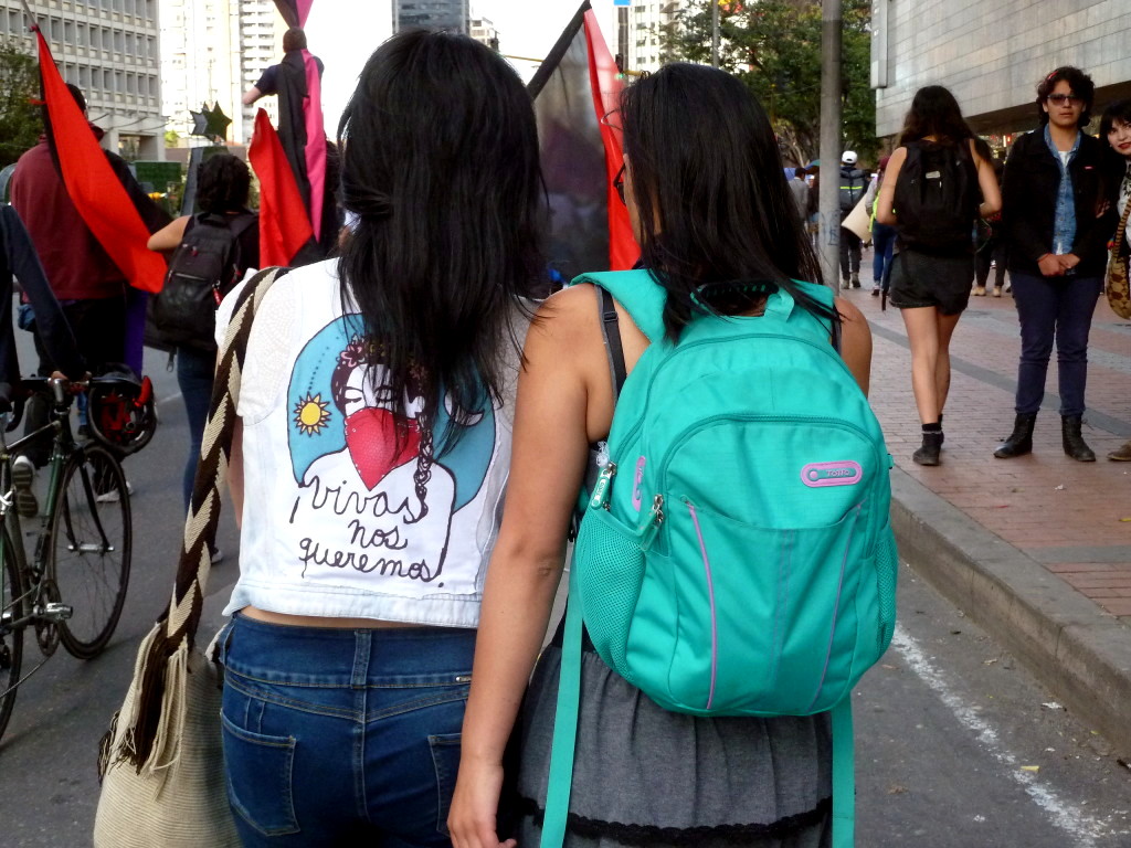 Dos mujeres aparecen de espaldas mientras caminan una junta a la otra en una manifestación. La camiseta de la jove de la izquierda dice "Vivas nos queremos". Foto: Marcela Zuluaga.