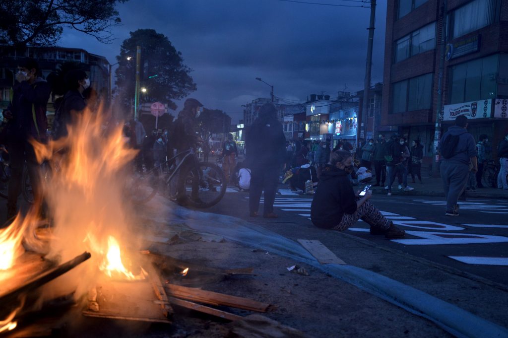 On the left, a bonfire; on the right, a group of young people block a road at sunset. Photo: Andrés Gómez