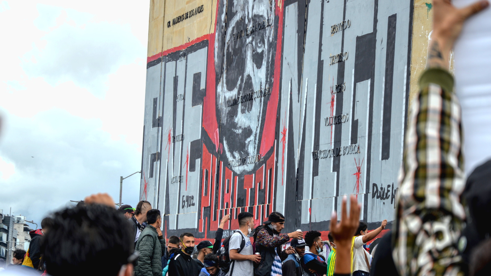 Jóvenes en una protesta junto al antiguo Monumento a los Héroes de Bogotá. Pintada en una de las paredes se lee "enemigo público" bajo una caricatura de Álvaro Uribe que lo muestra como un cráneo con sus facciones. Foto: Andrés Gómez