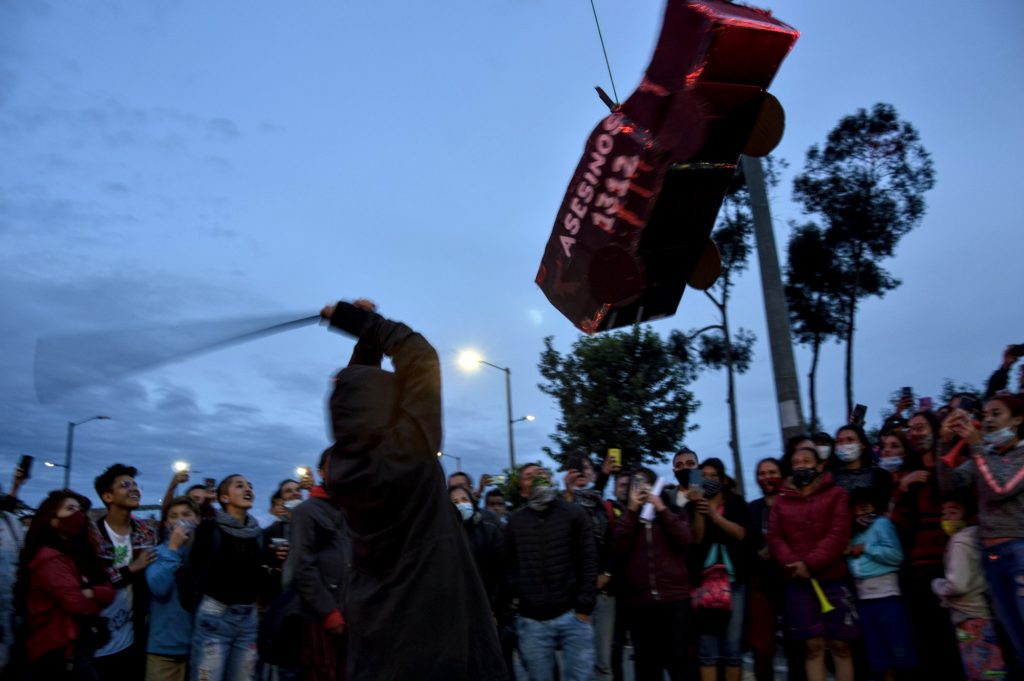 Una persona sostiene un palo sobre su cabeza e intenta golpear una piñata con forma de tanqueta que lleva escrito "asesinos 1312", alrededor un grupo de jóvenes le observa. Foto: Andrés Gómez